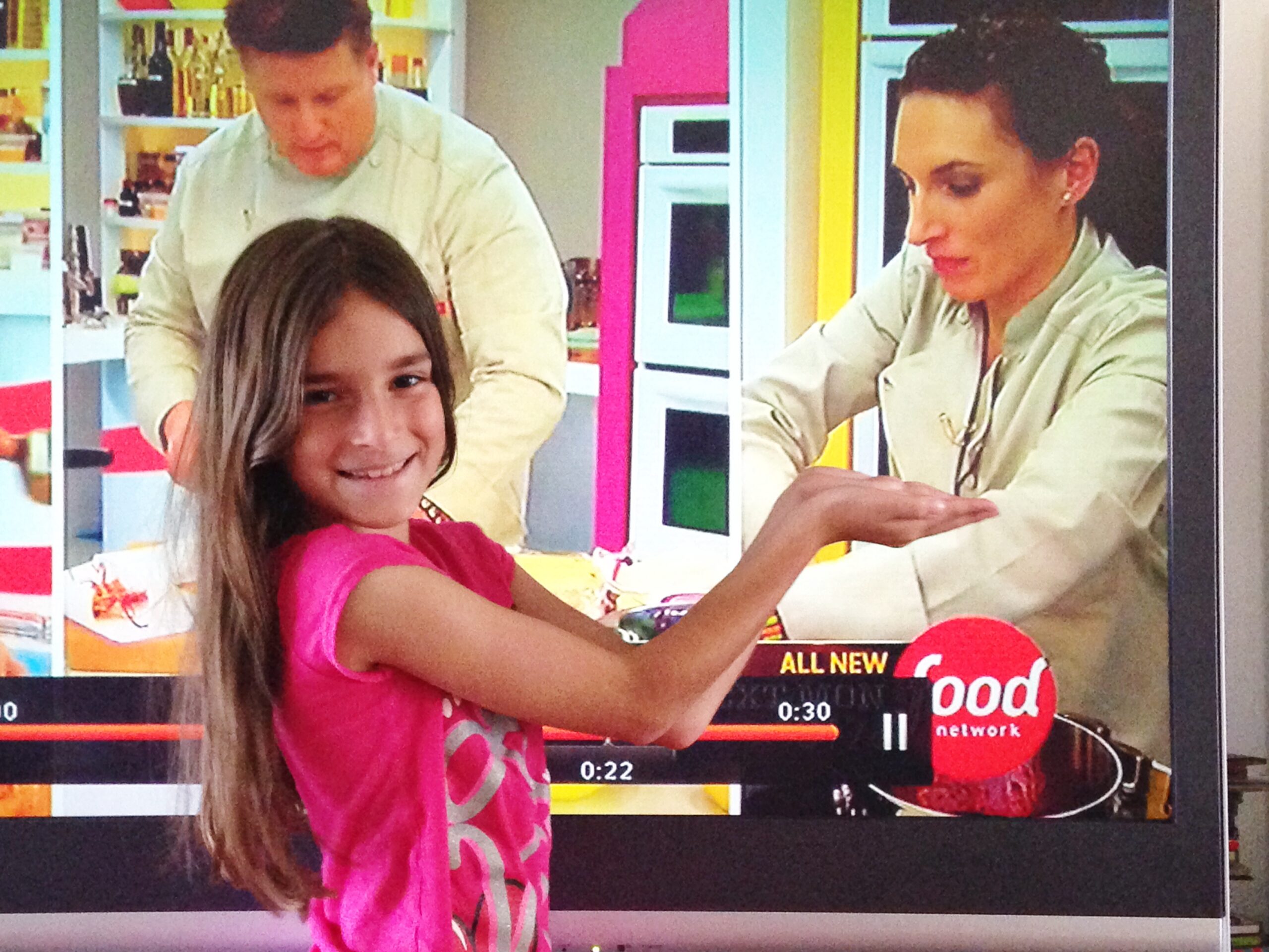 little girl proudly pointing at tv where her mom, Laura Fuentes is competing on food network